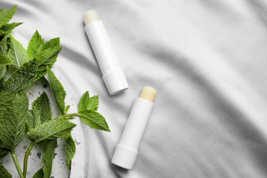 Photo of Hygienic lipsticks and mint leaves on light silk fabric, flat lay. Space for text