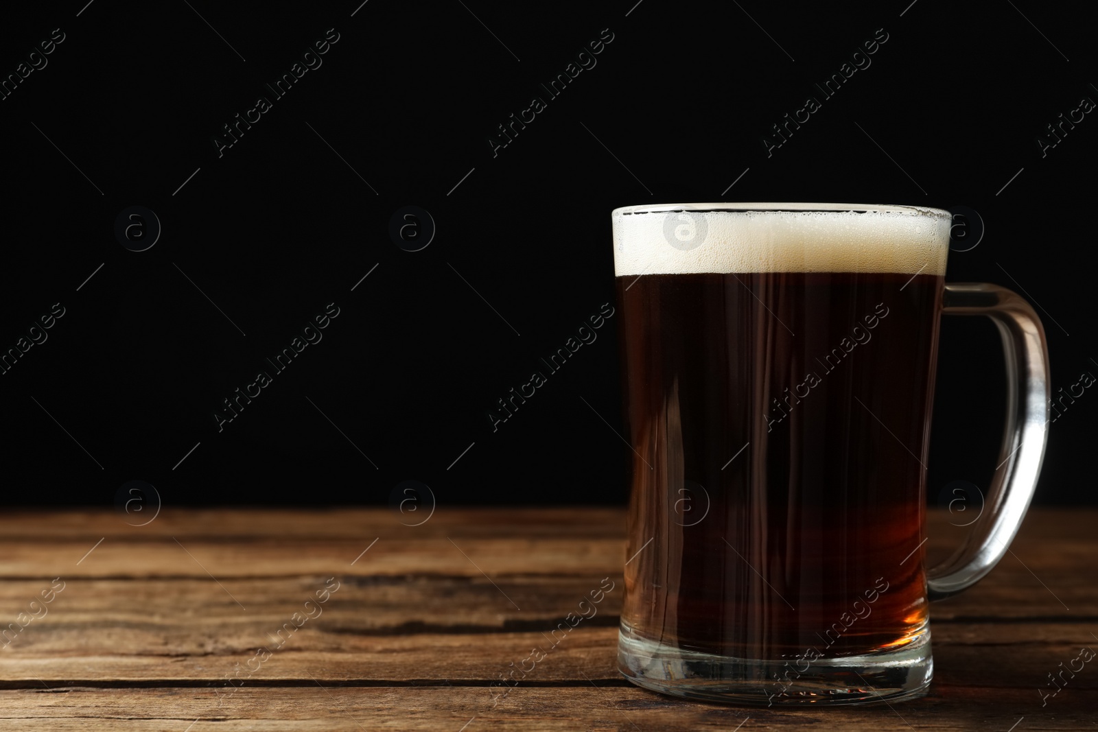 Photo of Mug of delicious kvass on wooden table against black background. Space for text
