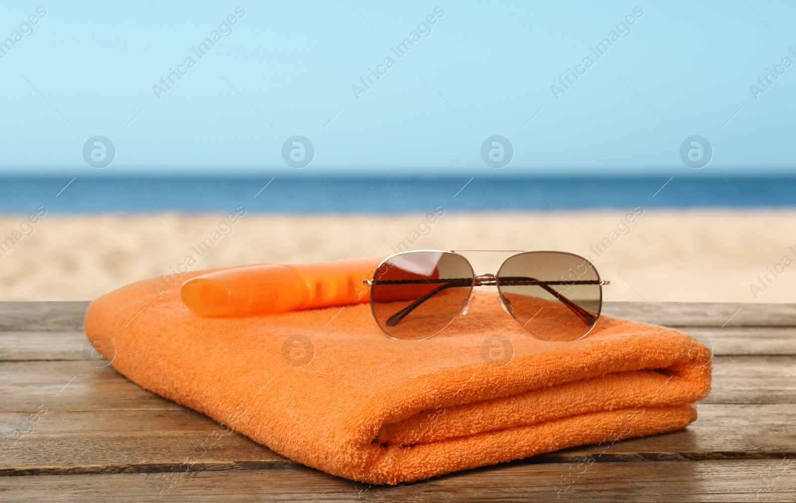 Image of Beach towel and sunglasses on wooden surface near seashore 