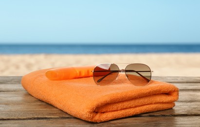 Beach towel and sunglasses on wooden surface near seashore 