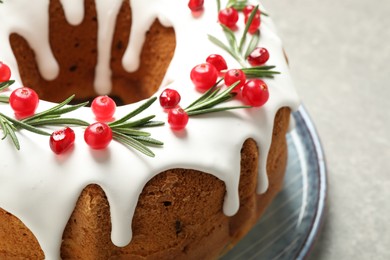 Traditional Christmas cake decorated with glaze, pomegranate seeds, cranberries and rosemary on light grey table, closeup