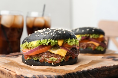 Photo of Tasty burgers with black buns on board, closeup