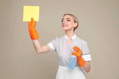 Photo of Young chambermaid with rag and detergent on color background