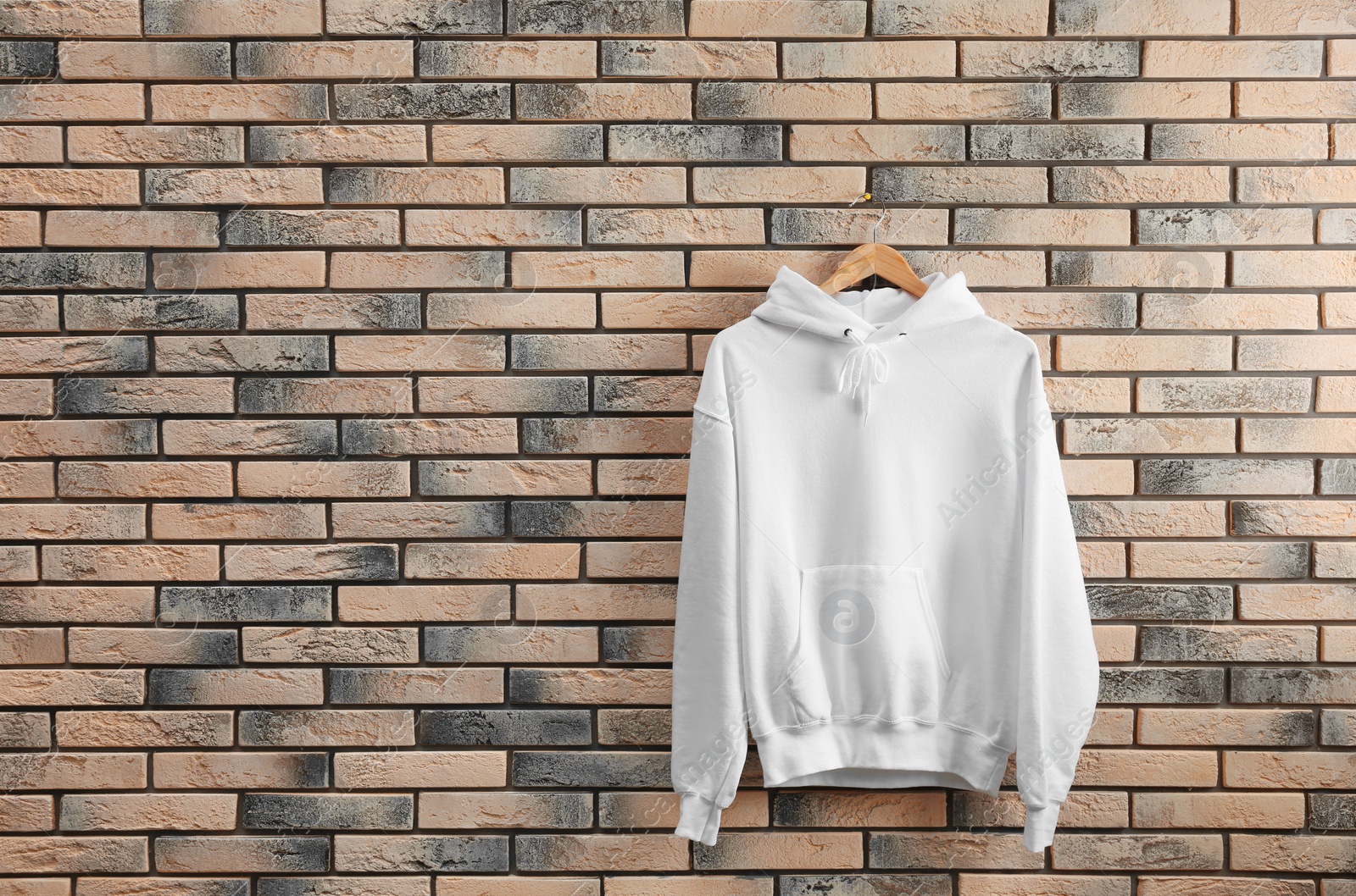 Photo of New hoodie sweater with hanger on brick wall. Mockup for design