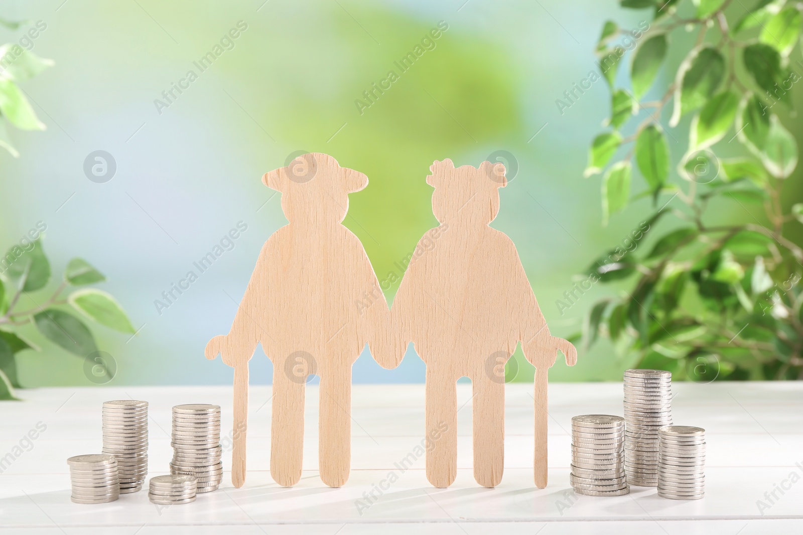 Photo of Pension savings. Figure of senior couple and stacked coins on white wooden table outdoors