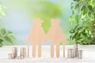 Pension savings. Figure of senior couple and stacked coins on white wooden table outdoors