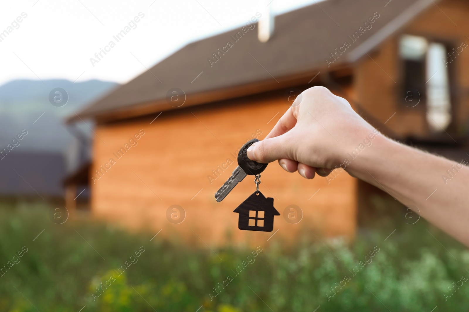 Photo of Real estate agent holding key and blurred house on background. Focus on hand