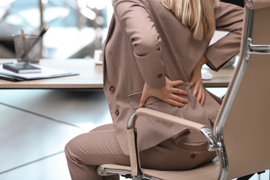 Photo of Young woman suffering from back pain in office, closeup