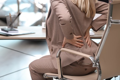 Young woman suffering from back pain in office, closeup