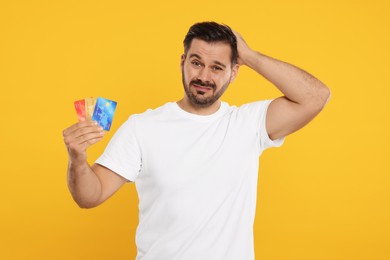 Confused man with credit cards on orange background. Debt problem