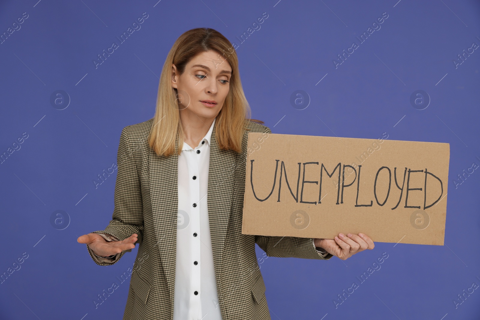 Photo of Confused woman holding sign with word Unemployed on violet background