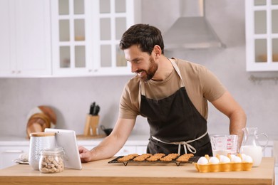 Man with freshly baked cookies watching online cooking course via tablet in kitchen