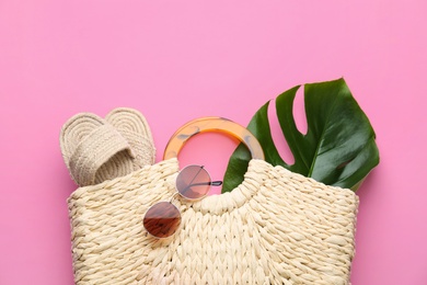 Elegant woman's straw bag with shoes, tropical leaf and sunglasses on pink background, top view