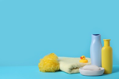 Photo of Baby cosmetic products, bath duck, sponge and towel on light blue background. Space for text