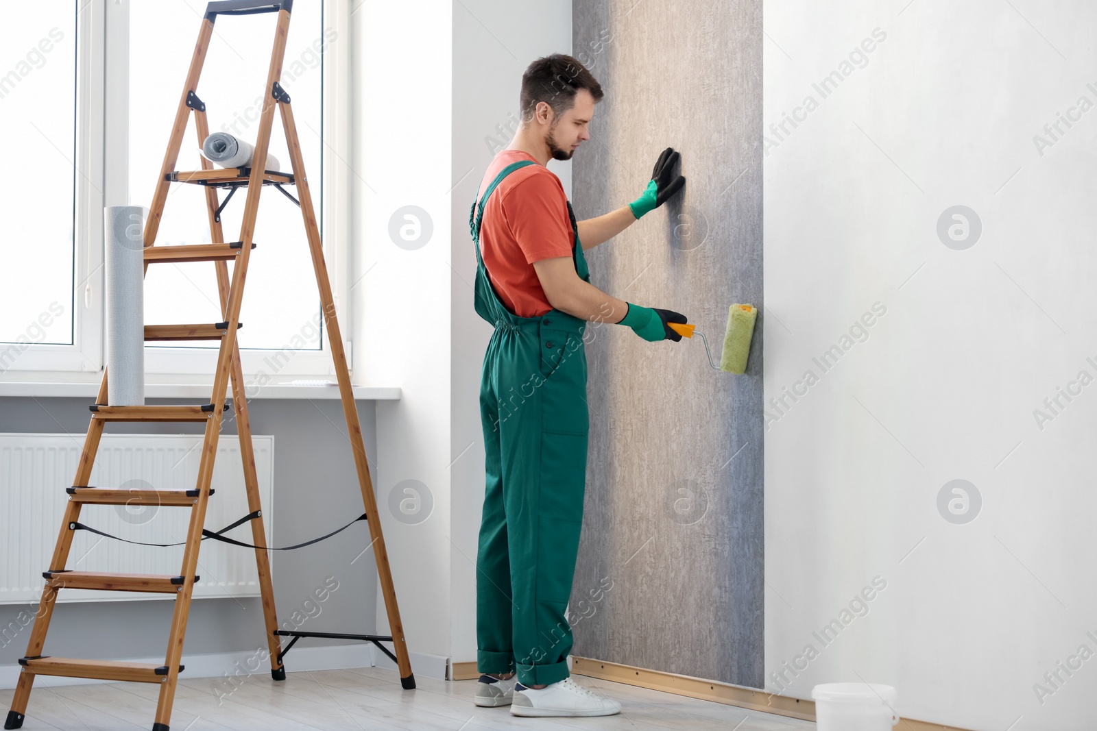 Photo of Man hanging stylish gray wallpaper in room