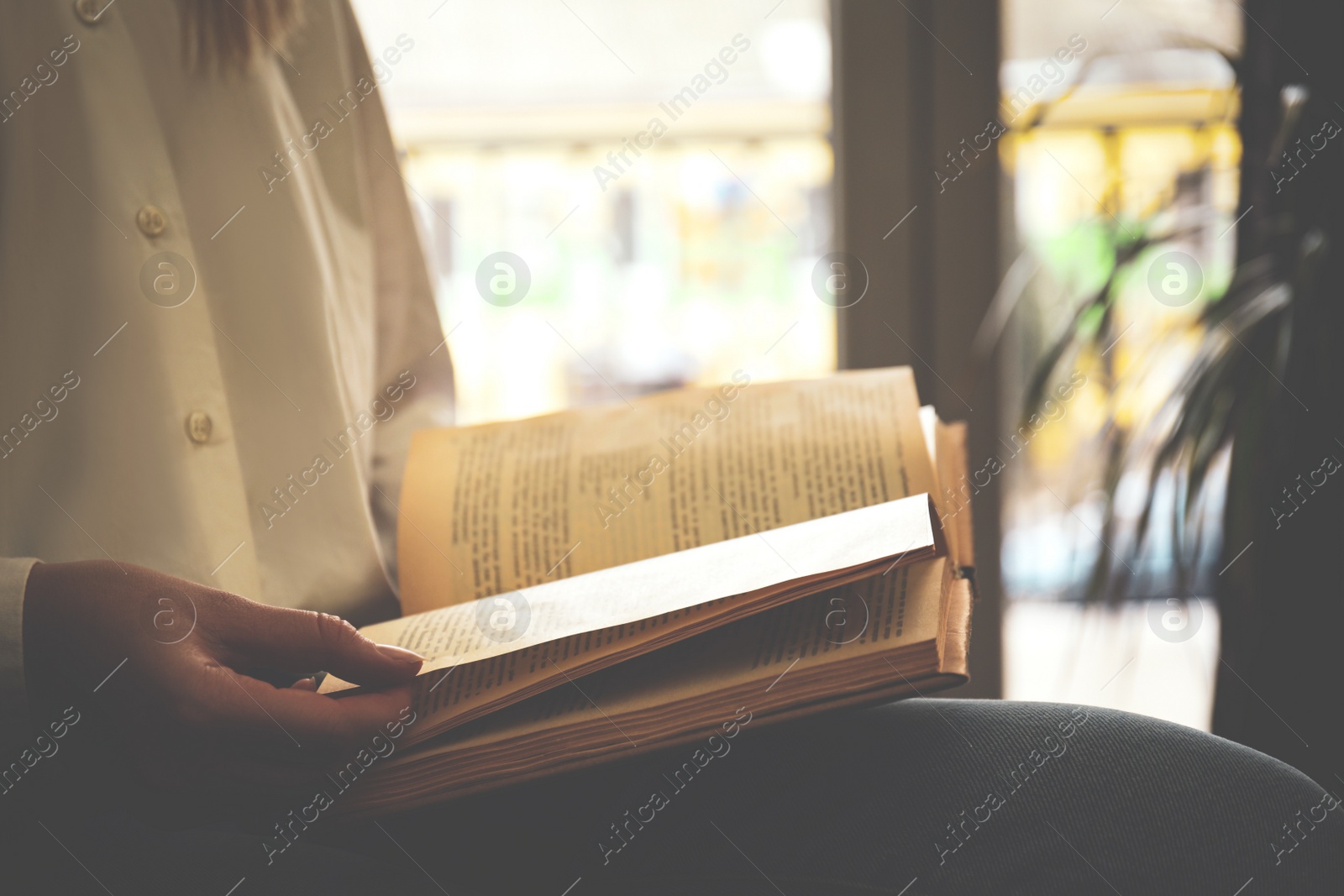 Photo of Woman reading book near window indoors, closeup