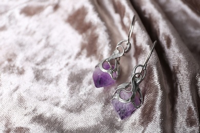Photo of Beautiful pair of silver earrings with amethyst gemstones on light fabric, closeup