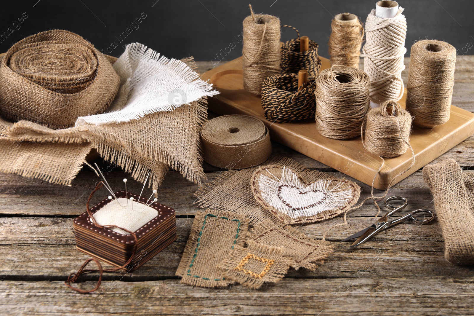 Photo of Pieces of burlap fabric, spools of twine and different sewing tools on wooden table