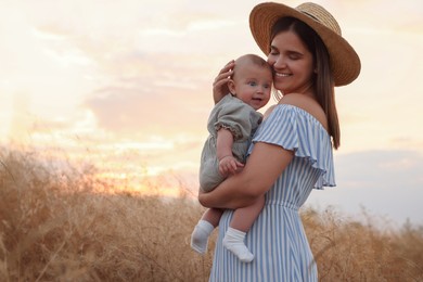 Photo of Happy mother with adorable baby in field at sunset, space for text