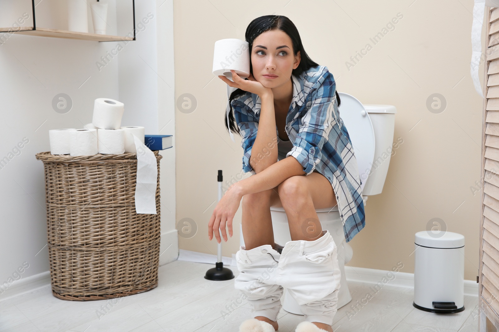 Photo of Woman with paper roll sitting on toilet bowl in bathroom