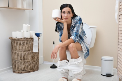 Photo of Woman with paper roll sitting on toilet bowl in bathroom