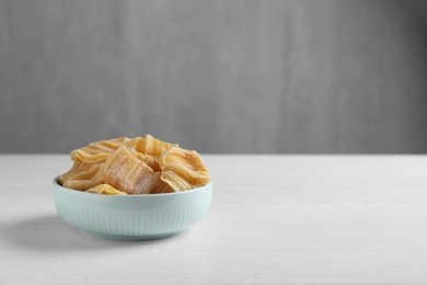 Delicious dried jackfruit slices in bowl on white wooden table. Space for text