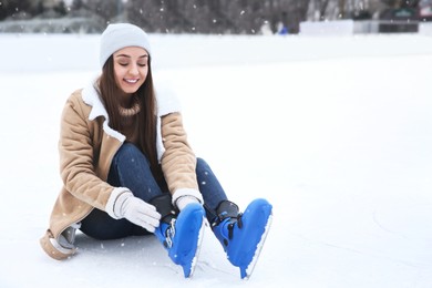 Happy woman wearing figure skates while sitting on ice rink outdoors. Space for text