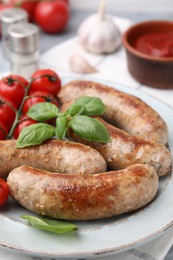 Photo of Plate with tasty homemade sausages, basil leaves and tomatoes on table, closeup