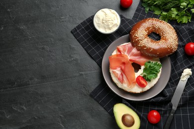 Delicious bagel with cream cheese, jamon, tomato and parsley on black table, flat lay. Space for text