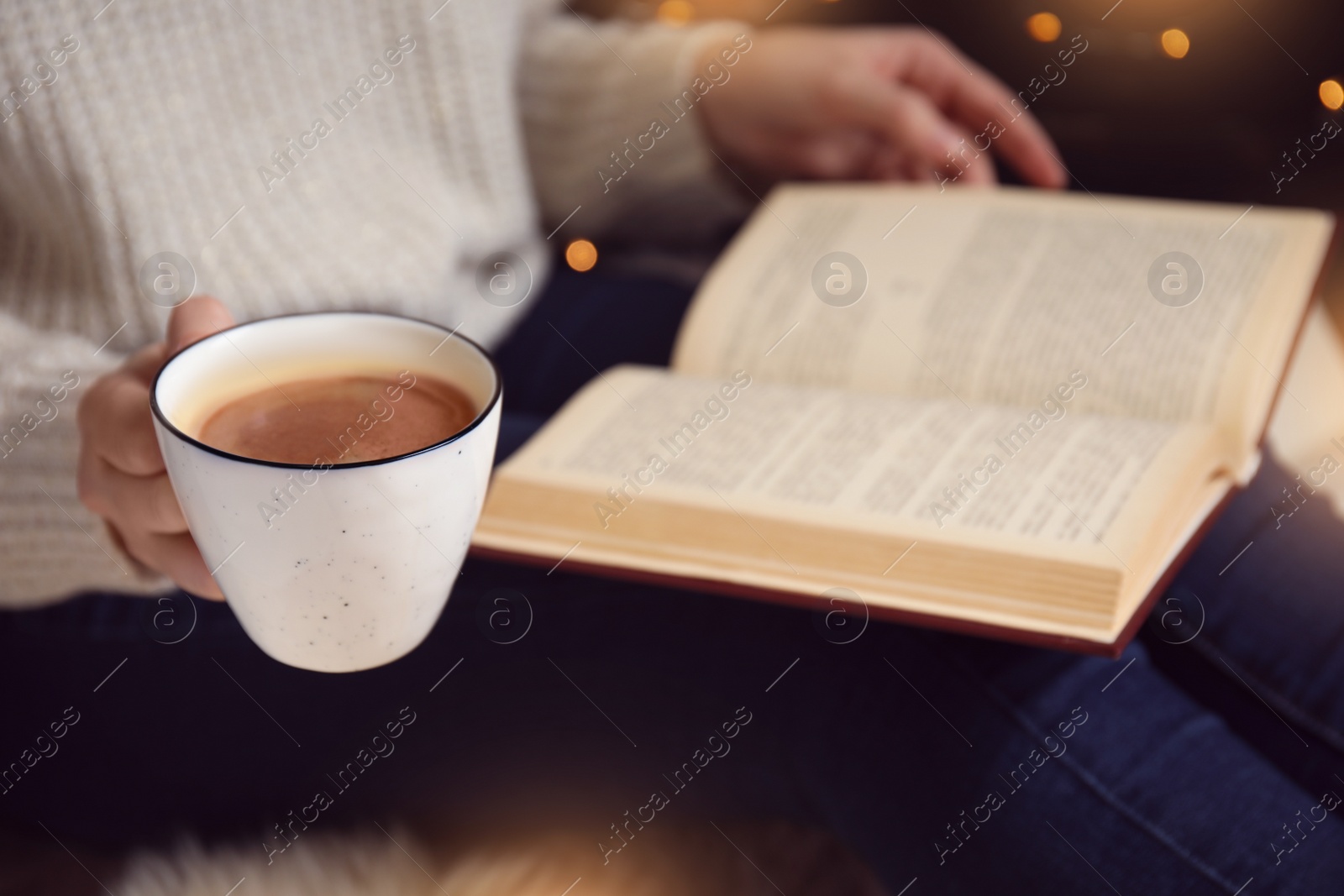 Photo of Woman with cup of coffee reading book at home, closeup