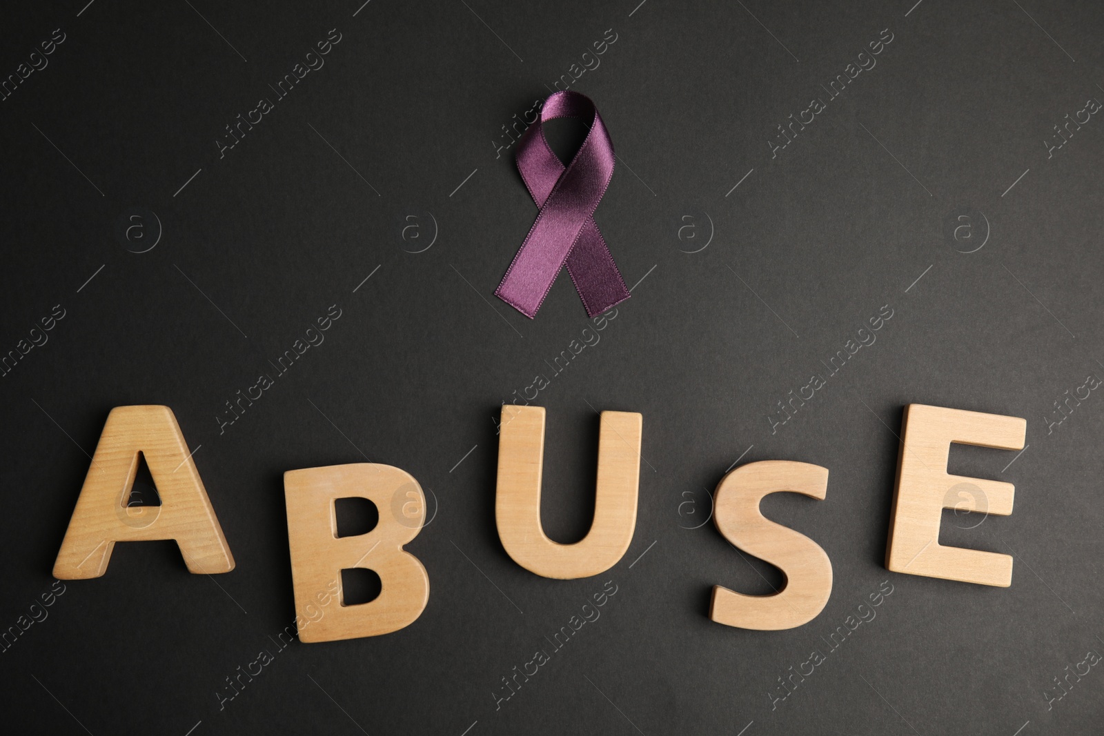 Photo of Purple ribbon and word ABUSE on black background, flat lay. Domestic violence awareness