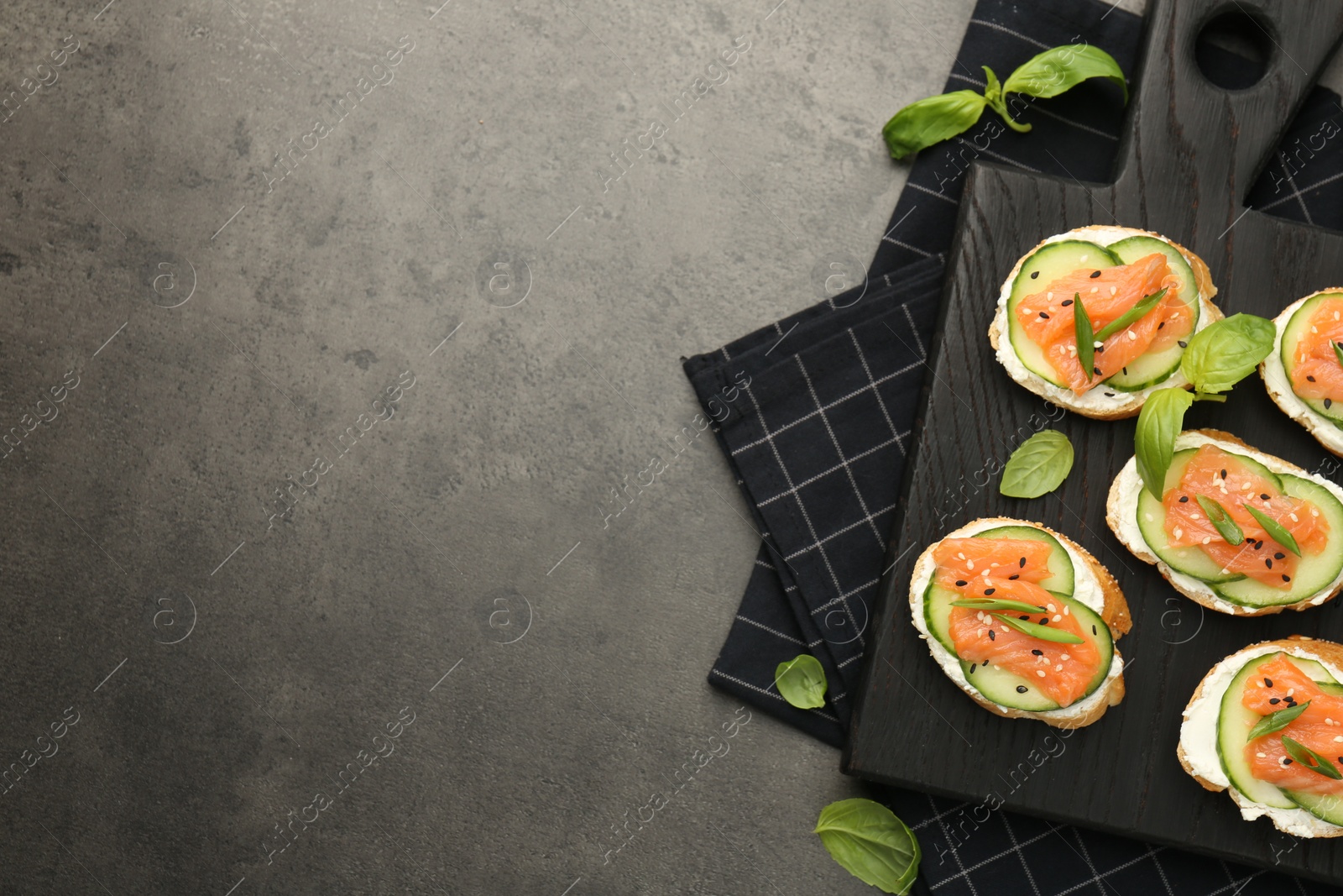 Photo of Tasty canapes with salmon, cucumber and cream cheese on grey table, top view. Space for text