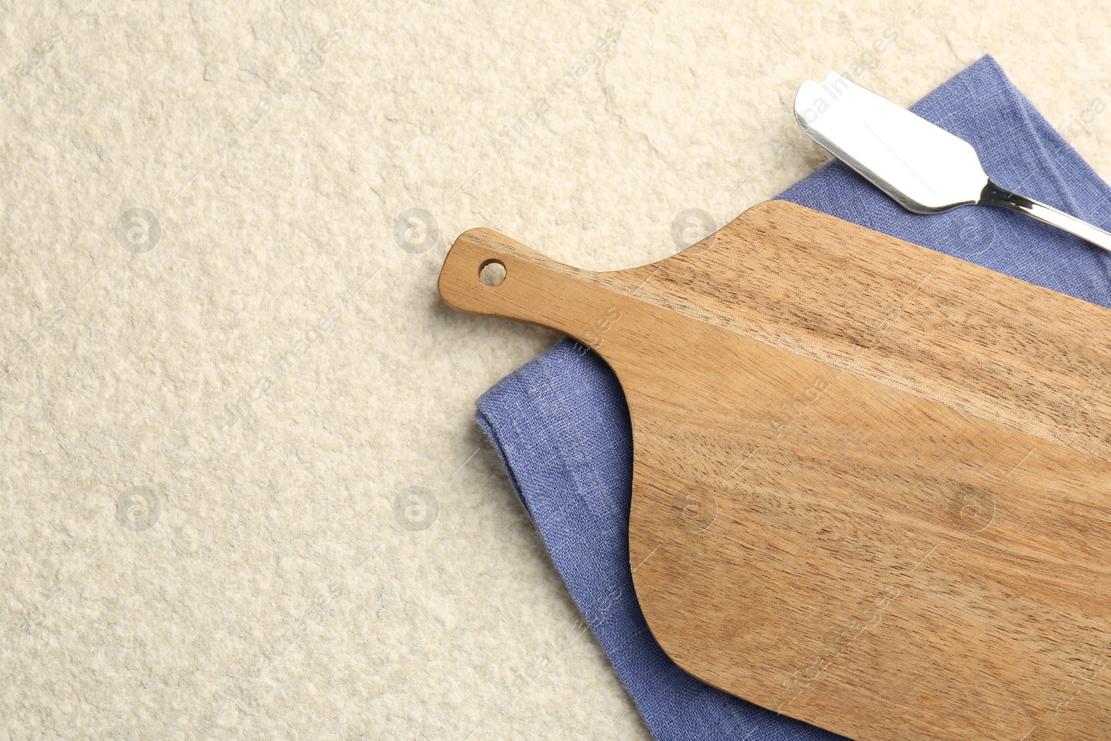 Photo of Wooden cutting board, napkin and butter knife on beige table, top view. Space for text