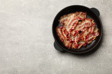 Delicious bacon slices in frying pan on grey table, top view. Space for text