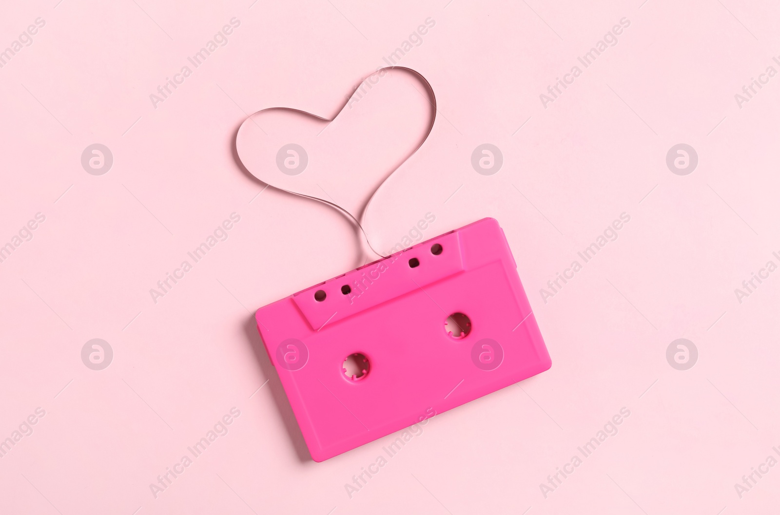 Photo of Music cassette and heart made with tape on pink background, top view. Listening love song