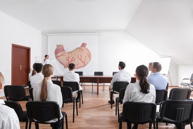 Image of Lecture in gastroenterology. Professors and doctors in conference room. Projection screen with illustration of stomach