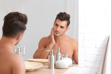 Young man with stubble ready for shaving near mirror in bathroom