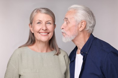 Senior man kissing his beloved woman on light grey background