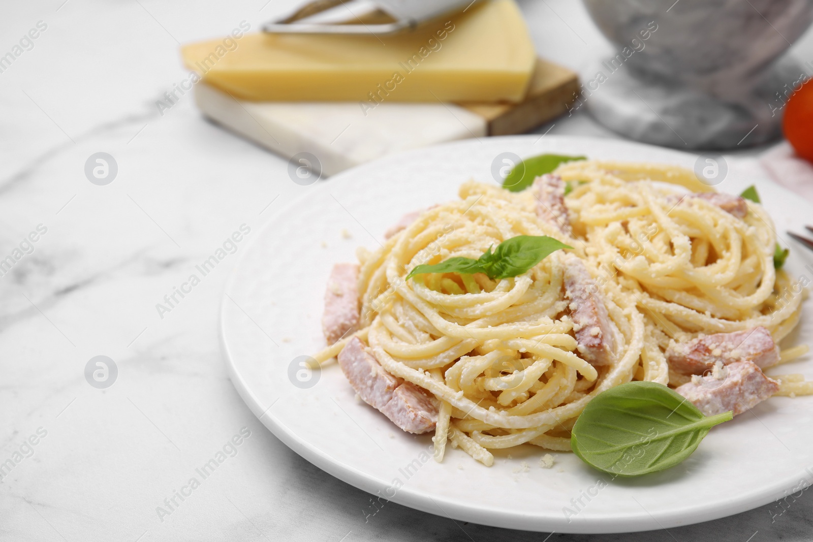 Photo of Plate of tasty pasta Carbonara with basil leaves on white marble table, closeup. Space for text