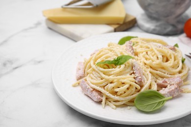 Plate of tasty pasta Carbonara with basil leaves on white marble table, closeup. Space for text