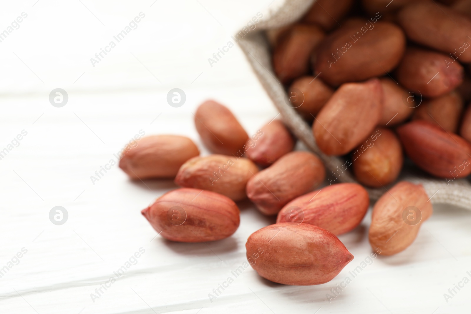 Photo of Fresh peanuts in sack on white wooden table, closeup
