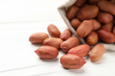 Photo of Fresh peanuts in sack on white wooden table, closeup