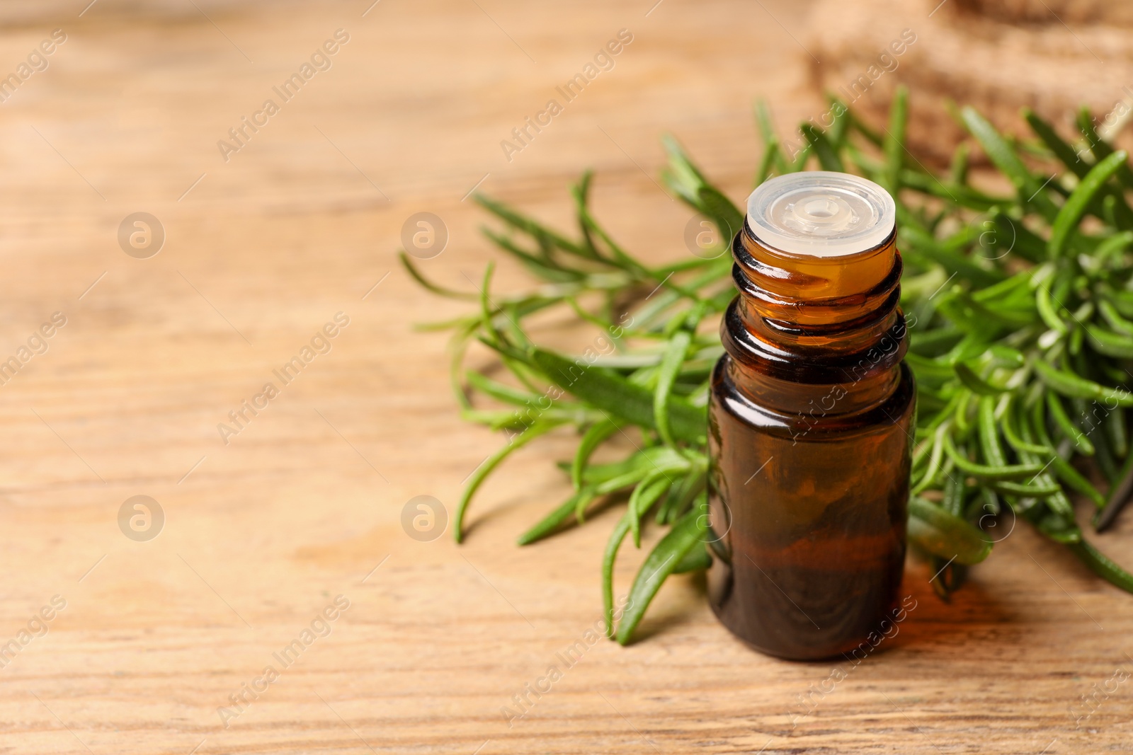 Photo of Bottle with essential oil and fresh rosemary on wooden table, space for text