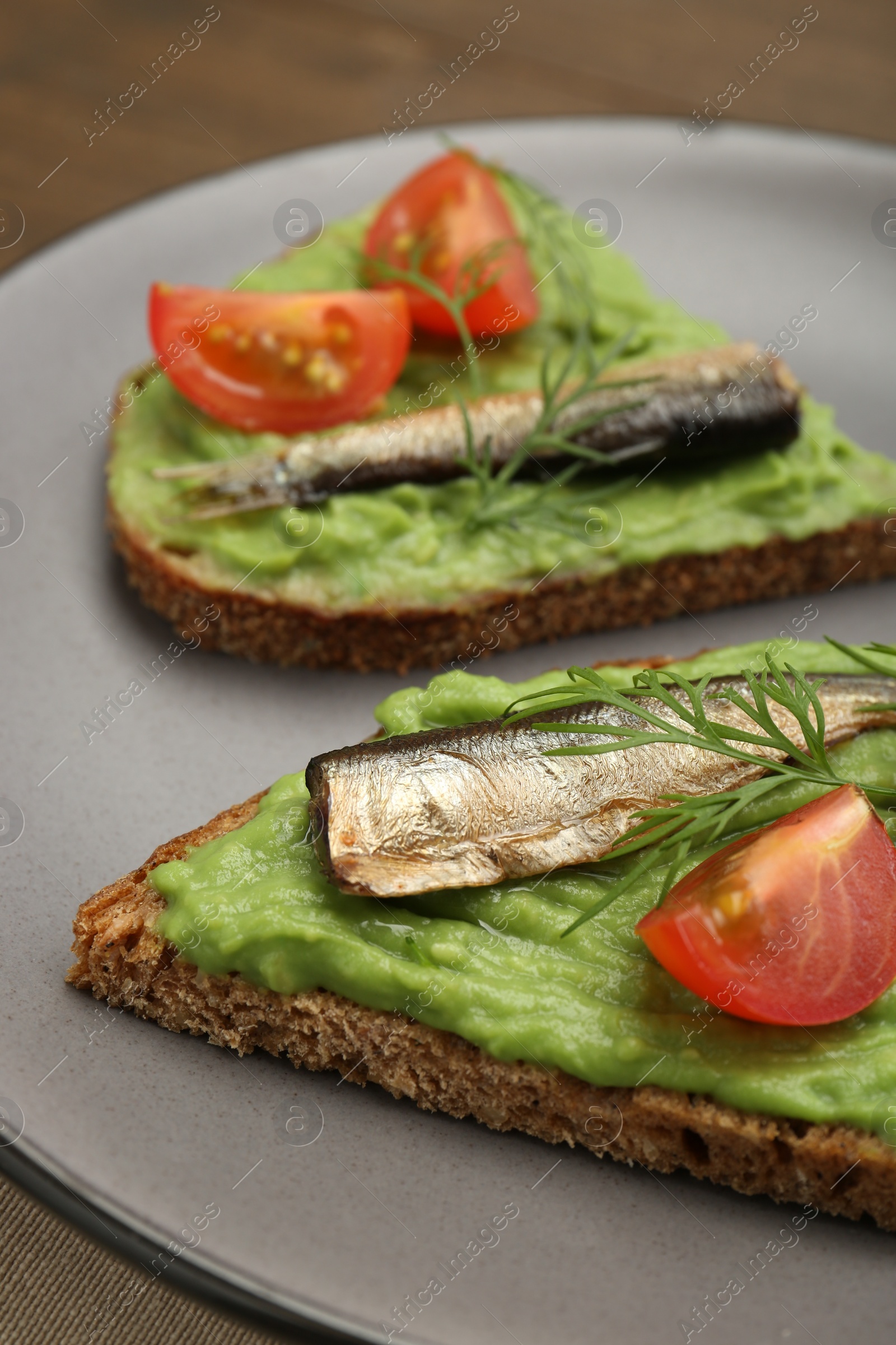Delicious sandwiches with sprats, tomatoes, avocado puree and dill on table, closeup Photo of Delicious sandwiches with sprats, tomatoes, avocado puree and dill on table, closeup