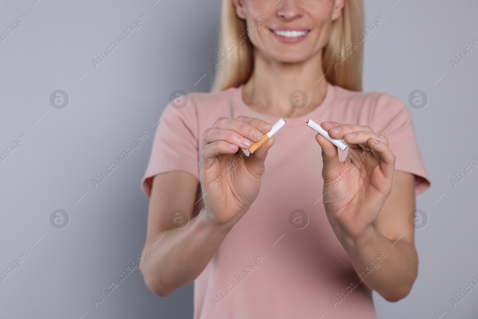 Photo of Woman with broken cigarette on light grey background, closeup. Stop smoking concept