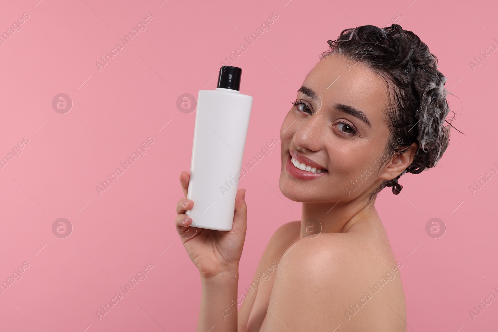 Photo of Washing hair. Portrait of beautiful happy woman with bottle on pink background. Space for text