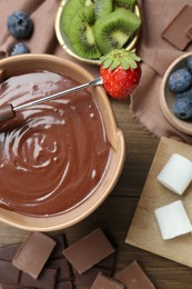 Photo of Fondue pot with melted chocolate, marshmallows, fresh kiwi, different berries and fork on wooden table, flat lay