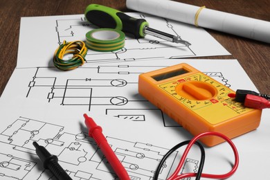 Photo of Wiring diagrams, digital multimeter and tools on wooden table, closeup