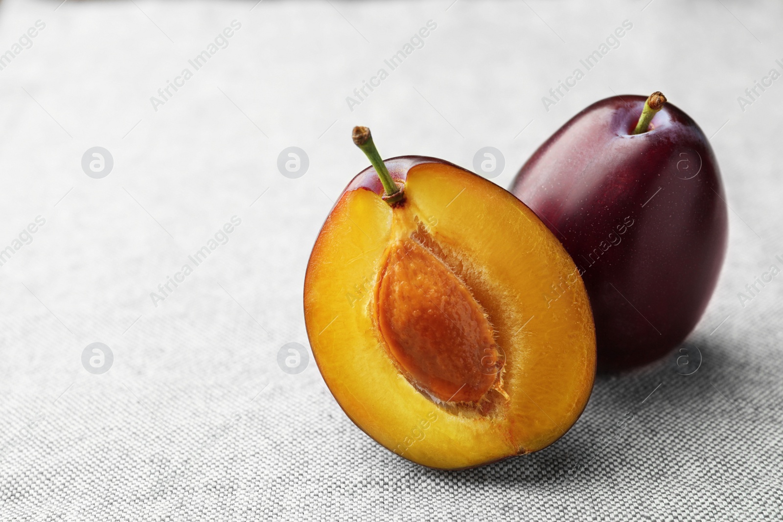 Photo of Tasty ripe plums on light fabric, closeup. Space for text