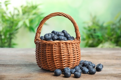 Wicker basket with fresh blueberries on wooden table against blurred green background